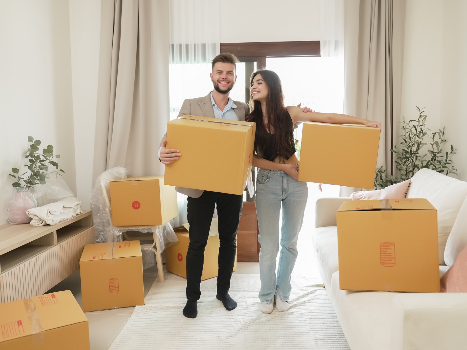 Happy couple man and woman carrying boxes together into their new home. Happy heterosexual couple carrying cardboard boxes on moving day. Homebuying. Relocation